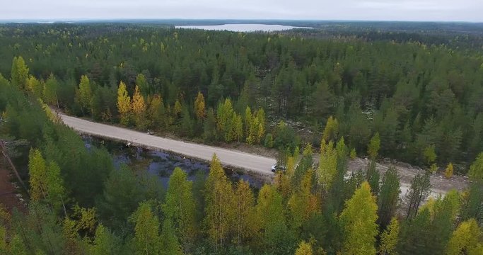 Vehicle is on the autumn country road. Driving through the evergreen forest with lakes. Top view from drone. Karelia, Russia