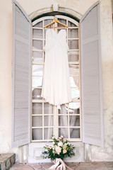 A white bridal dress on wooden shoulders, against the window. Artwork
