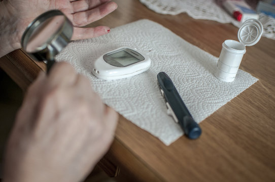 anziana malata di diabete testa la glicemia del sangue con una lente di ingrandimento