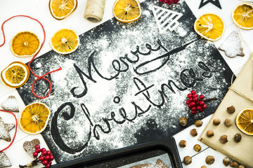 inscription Christmas on a black board sprinkled with flour among the Christmas decor, ginger biscuits and dried oranges