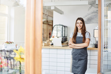 Young lady entrepreneur running a successful small cafe. Standing in front of coffee machine with arms crossed.