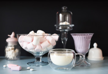 White desserts on black and blue background. Marshmellow, smoothie and milk in glass utensils