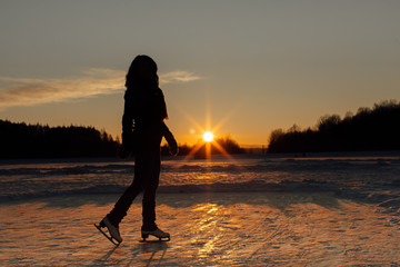 A silhouette of a woman with ice skates at sunset