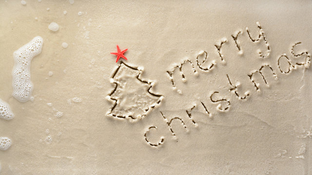 Holiday background - merry Christmas and tree with starfish drawn on a sandy beach