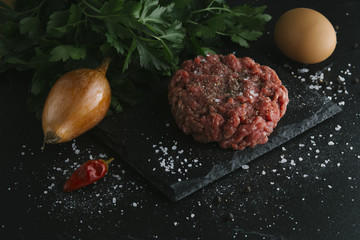 Tartare steak. Beef raw chopped meat with spices, herbs and egg yolk. Fresh, spicy, delicious, gourmet meal on dark background with copy space, close-up