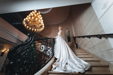 Beautiful woman in a white dress with long train is climbs up the stairs in a classic interior. 