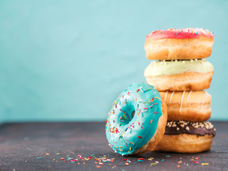 Stack of assorted donuts on black and blue cement background. Blue glazed doughnut with sprinkles on foreground. Copy space. Shallow DOF - obrazy, fototapety, plakaty