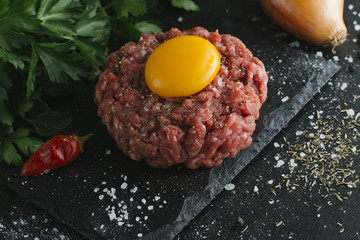 Tartare steak. Beef raw chopped meat with spices, herbs and egg yolk. Fresh, spicy, delicious, gourmet meal on dark background with copy space, close-up