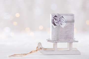 Little pretty gift box on toy white sled on light bokeh background