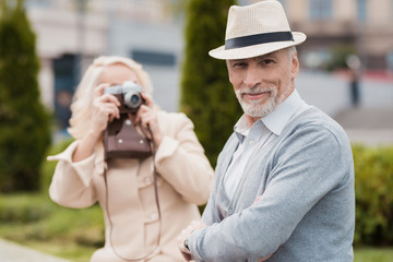 An elderly couple is sitting on the edge of a flower bed. They take pictures of each other on a vintage film camera