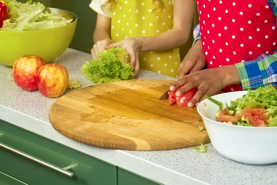 Hands of kid cutting tomato. Fresh vegetable on cooking board.