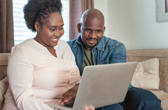 Smiling African couple sitting on a sofa using a laptop