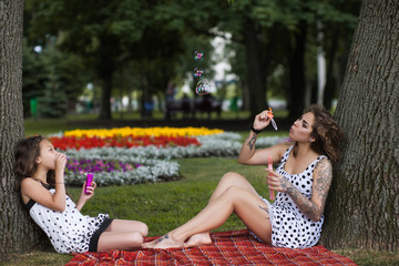 Fun activity on nature. Forever young. Stylish girls with soap bubbles, park background. Happy summer life, creative family picnic