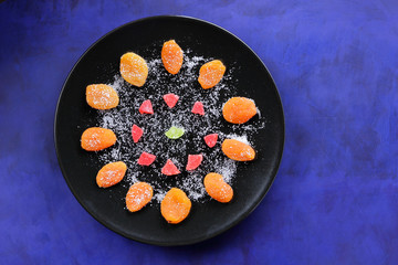 Dried apricots, candied fruits in sugar on a black plate on a dark blue background