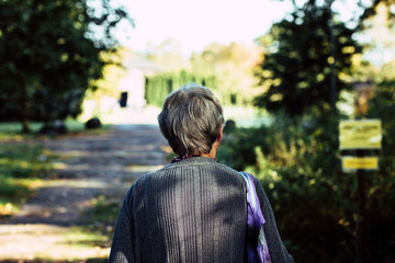 healthy elderly woman with grey hair from the back walking through nature
