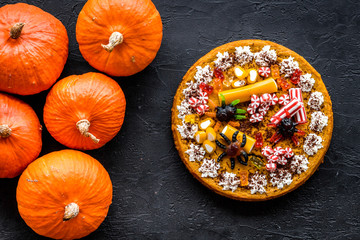 Homemade pie for halloween decorated gummy spiders among pumpkins on black background top view