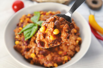 Spoon with chili con carne over plate on table, closeup