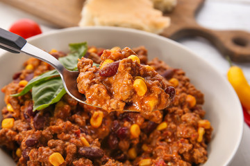 Spoon with chili con carne over plate on table, closeup