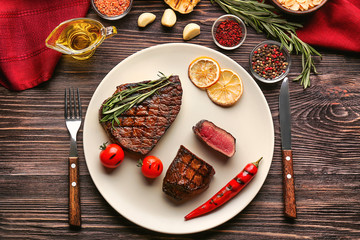 Plate with yummy grilled steaks on wooden table