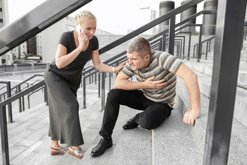 Woman calling ambulance for man suffering from heart attack outdoors © Africa Studio