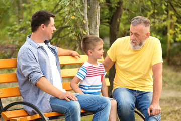 Cute boy with dad and grandfather sitting on bench in park