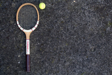 Old vintage wooden tennis racket on isolated stone background with green ball.