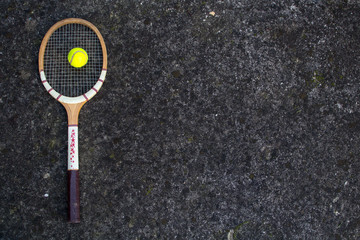Old vintage wooden tennis racket on isolated stone background with green ball.