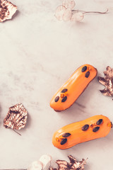 Two orange glazed eclairs and gold colored leaves on white marble background. Stylish fall season flatlay. Copy space for text