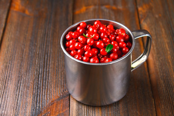 Cowberry, foxberry, cranberry, lingonberry in an aluminum mug on a brown wooden table.