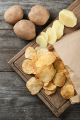 Board with crispy potato chips on wooden table