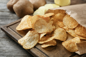 Board with crispy potato chips on wooden table