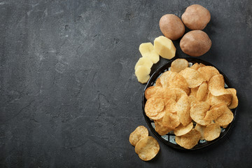 Plate with yummy crispy potato chips on dark background