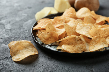 Plate with yummy crispy potato chips on dark background