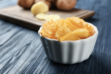 Bowl with yummy crispy potato chips on wooden table