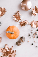 Blurred fall season flatlay on white marble background. Little pumkin, rose gold painted leaves. 