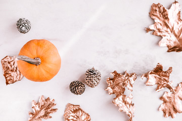 Stylish fall season flatlay on white marble background. Little pumkin, rose gold painted leaves. Copy space for text