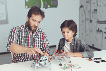 A man helps a boy with a robot assembly. The boy looks carefully as a man collects a robot