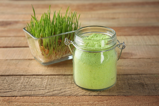 Jar with natural wheat grass powder and sprouts in bowl on wooden background