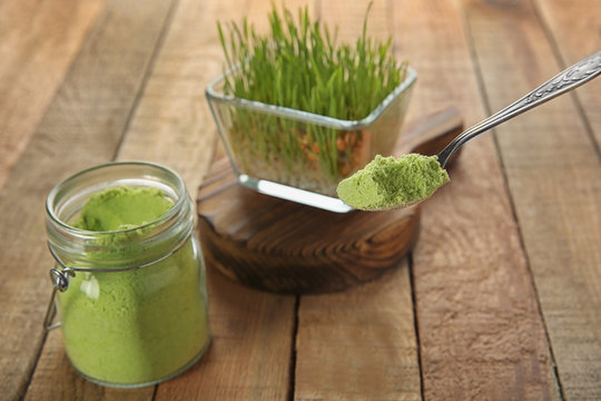 Natural wheat grass powder in spoon and glass jar on wooden background