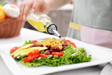 Woman pouring olive oil onto vegetable salad in kitchen