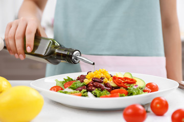 Woman pouring olive oil onto vegetable salad in kitchen