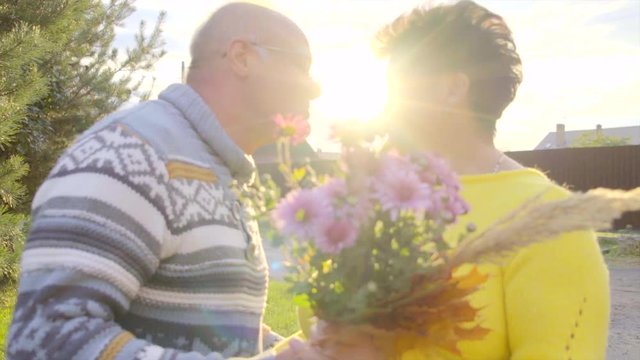 Elderly man is giving flowers to his lady and they are kissing at sunset