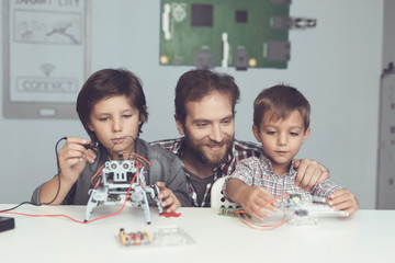 A man and two boys construct a robot. The man helps the boys with the assembly