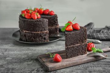 Board with piece of delicious chocolate cake on table