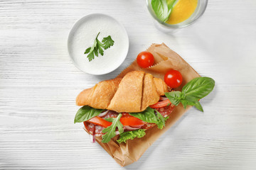 Delicious croissant sandwich with sausage and vegetables on paper