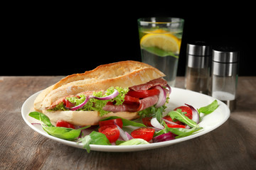 Plate with delicious sausage sandwich on table