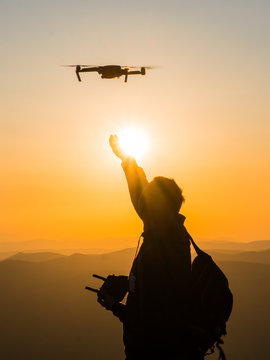 Silhouette of young man catching drone at sunset for photos and video making - Happy man having fun with new technology trends in mountains