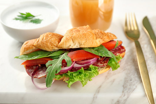 Delicious croissant sandwich with sausage and vegetables on stone board