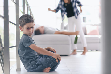 Little boy with bruise sitting on floor while his parents fighting on background. Domestic violence...