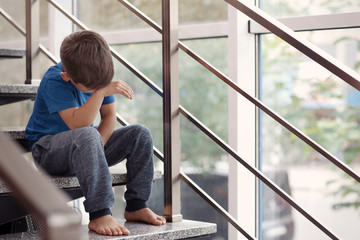 Little boy crying on stairs indoors. Domestic violence concept
